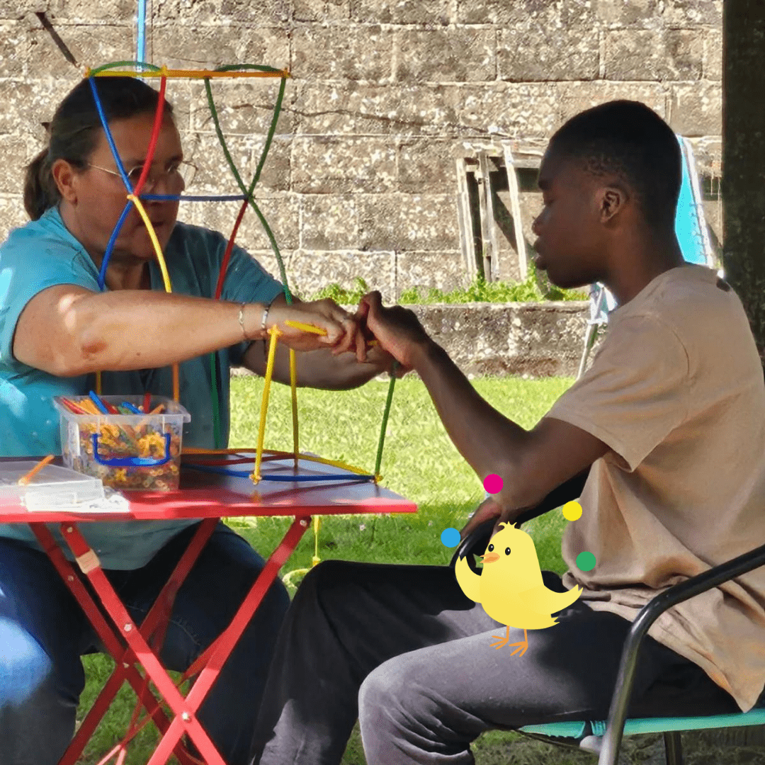 Une bénévole de l'association Tombée du Nid aide un jeune en situation de handicap à construire une structure avec des bâtonnets, montrant l'impact positif de l'application Le Cœur du Nid.