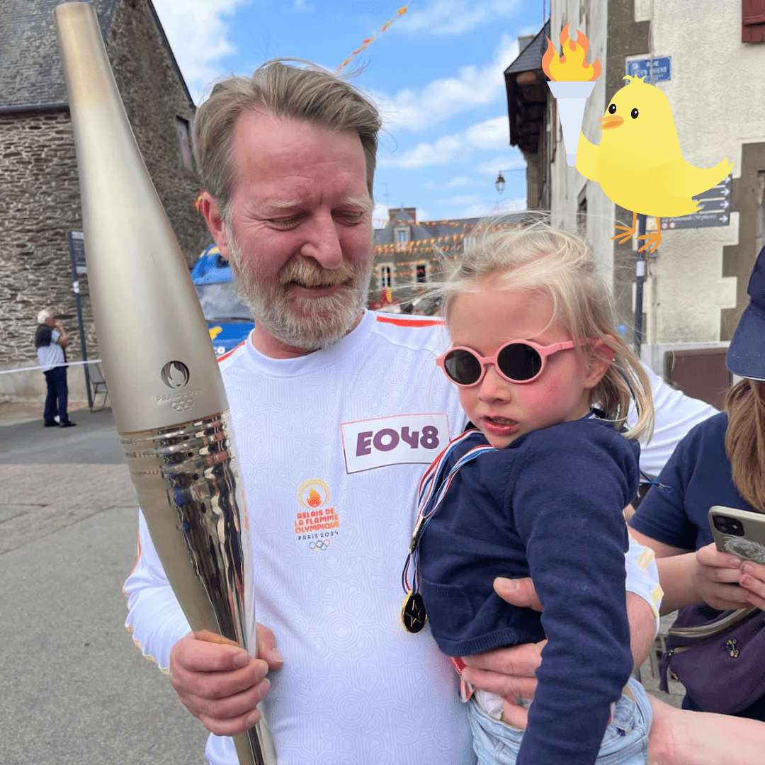 Un adulte porte la flamme olympique, accompagné d'un enfant portant des lunettes de soleil, lors du relais de la flamme pour les Jeux Olympiques de Paris 2024.